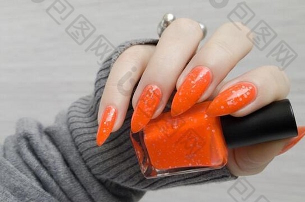 有着长长指甲和橙色姜黄色指甲的女人手上拿着一瓶指甲油