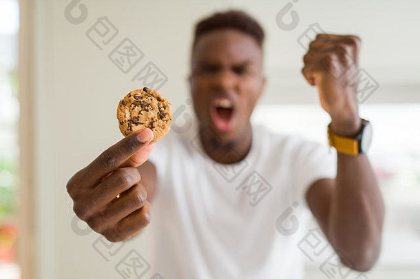 年轻的非洲裔美国人正在吃巧克力片饼干，他愤怒地叫喊着，发疯了，举起手叫喊着，愤怒的自负