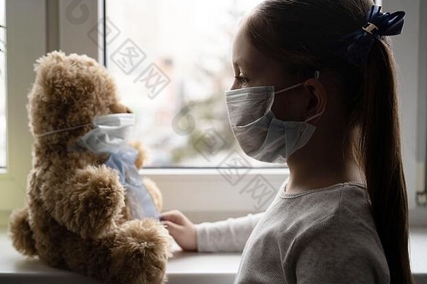 悲伤的孩子和他的泰迪熊都戴着防护面具。儿童与疾病新冠病毒-2019疾病概念