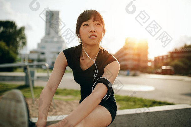 健身女士在训练前伸展双腿。美丽的中国运动员在城市公园户外运动。