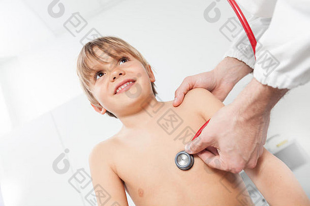 一位儿童医生在儿科病房用听诊器听诊一个微笑男孩的胸部。