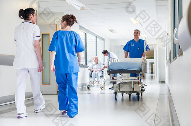 男护士在医院走廊推担架床，与医生和资深女患者在一起