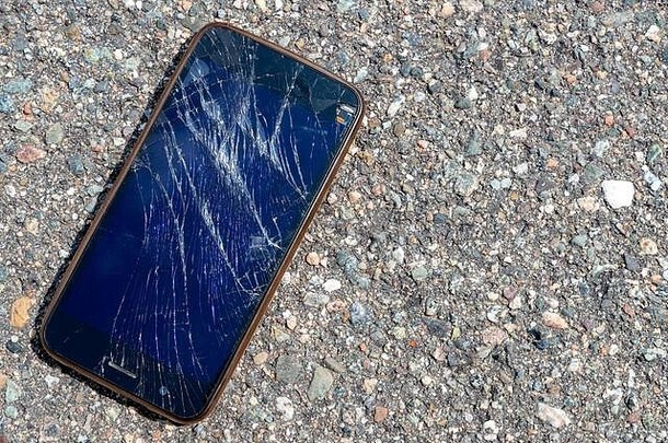 一部破碎的手机躺在柏油路上。手机屏幕被打碎了。电话无法识别。