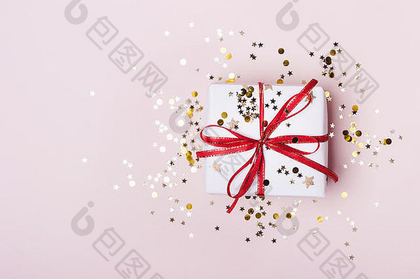 带有红结和粉红色粉彩背景上闪闪发光的五彩纸屑的礼品盒。节日的概念。