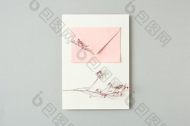 浅灰色背景上的花枝和纸信封制作的节日贺卡。
