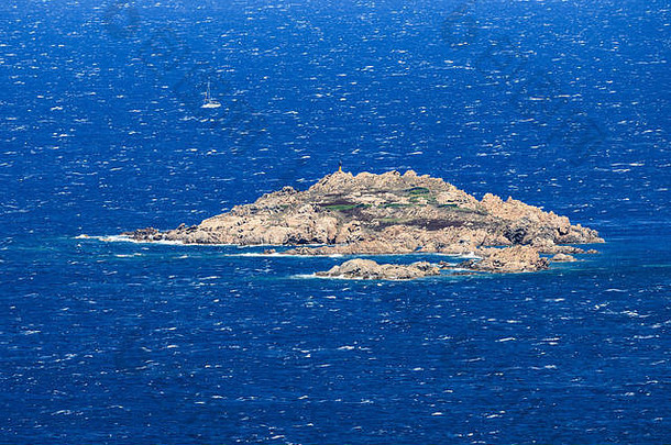 从上面俯瞰，一个波涛汹涌的大海，背景是一个岩石小岛和一艘帆船。撒丁岛，意大利。