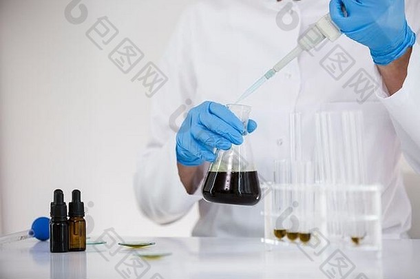 一位女科学家在实验室里研究从植物中提取的CBD油。她正在警告蓝色的光芒，并把碗里的油撕成碎片