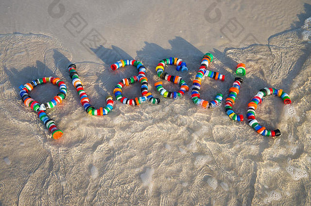 在一个光滑的海滩上，用废弃的瓶盖在一个五颜六色的单词中制作塑料宣传信息