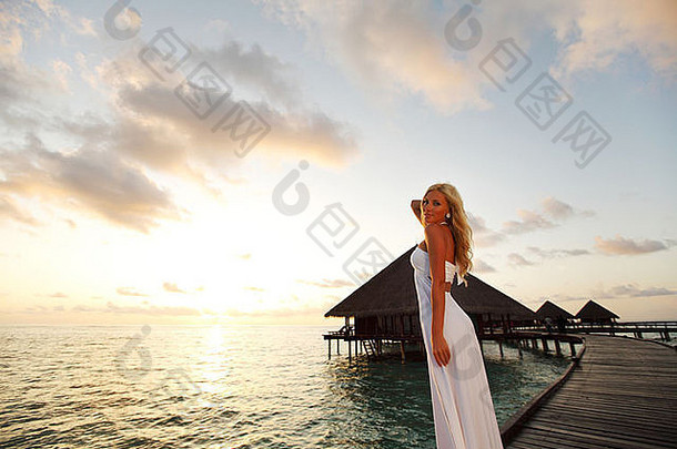 一个穿着裙子的女人在桥上回家，背景是大海和马尔代夫的日落