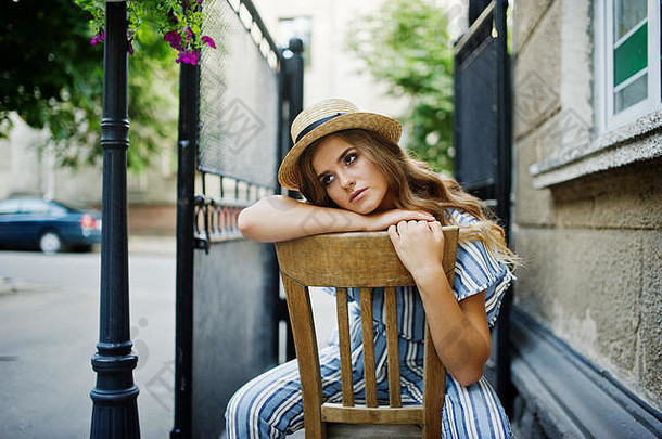 一位穿着条纹衣服、戴着帽子的年轻女子坐在户外的椅子上摆姿势的肖像。