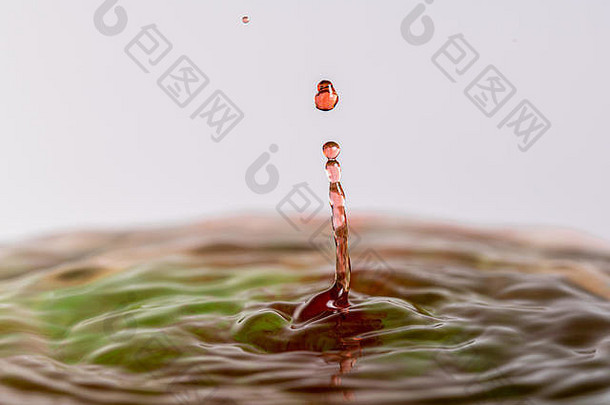 一个红色和绿色水滴在浅色白灰色背景下溅入水中的特写微距摄影