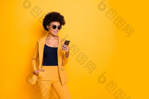 一位迷人、酷炫的美国黑人女士的肖像使用她的智能手机在博客式帖子中与粉丝交流评论穿着时尚的衣服和裤子
