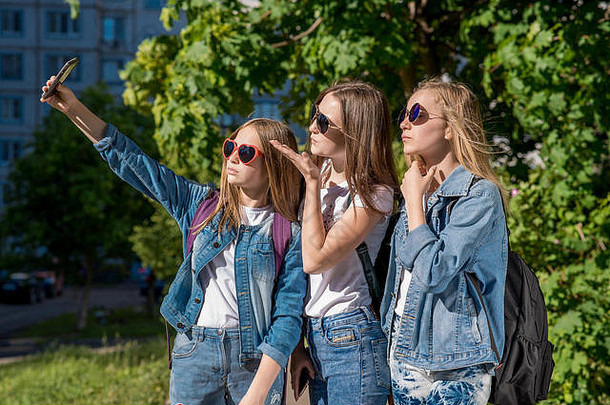 十几岁的女孩夏天在户外使<strong>照片</strong>人电话穿时尚的牛仔裤衣服阳光明媚的保护眼镜十几岁的女孩金发女郎背包支持