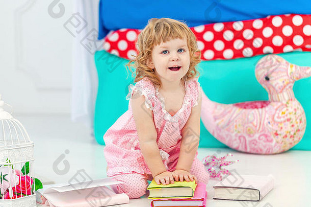可爱的卷曲的女孩粉红色的睡衣看书微笑坐着地板上孩子们的卧室相机