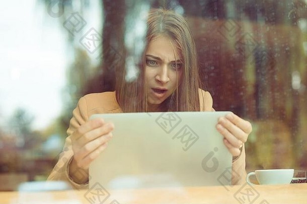 震惊了女人持有电脑移动PC平板电脑屏幕惊讶咖啡商店