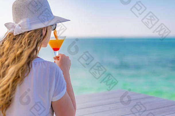 女人在海边放松，热带度假和度假理念。戴着白帽子拿着鸡尾酒的女人。