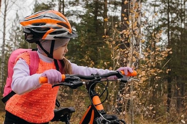 一个白人孩子在秋天公园里骑自行车散步。小女孩在森林里骑着<strong>黑橙</strong>色的自行车。这孩子去做自行车运动。骑自行车的运动骑乘