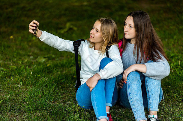 十几岁的女孩夏天城市公园坐草照片智能手机背包概念学校友谊情感构成电话