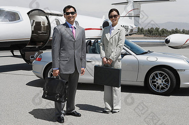 中年女商人和中年商人站在跑道上私人飞机前的肖像。