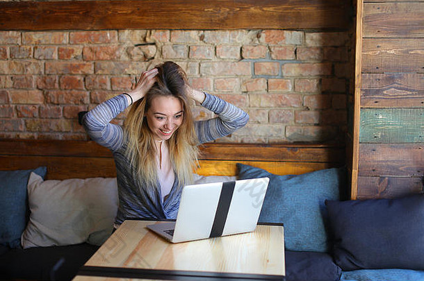 一位女士坐在桌子旁舒适的咖啡馆里，端着一杯咖啡，用笔记本电脑进行交流。