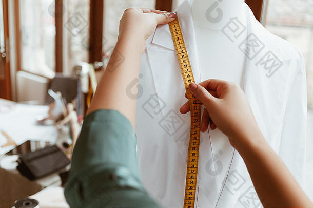 最重要的是尺寸合适。女设计师正在用卷尺测量白色衬衫，特写镜头