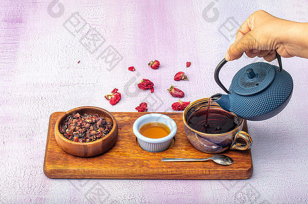 玫瑰果冲茶，茶道，一杯新鲜的水果和花草茶，黑暗的心情。热水从壶里倒进一杯茶