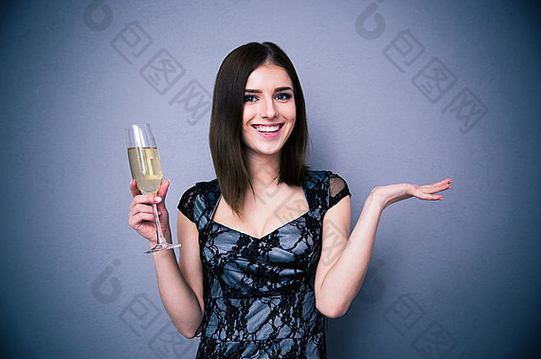 微笑漂亮的女人持有玻璃香槟灰色的背景相机穿衣服