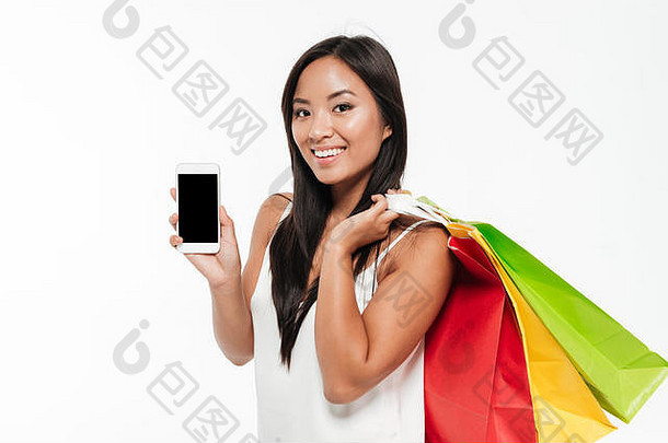 肖像快乐的休闲亚洲女人显示空白屏幕移动电话站色彩斑斓的购物袋孤立的白色背景