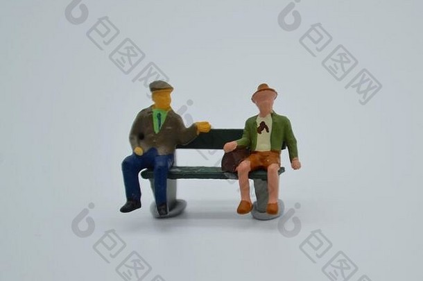 在新冠肺炎流行期间，两位老人在公园长椅上练习社交距离的微型雕像场景