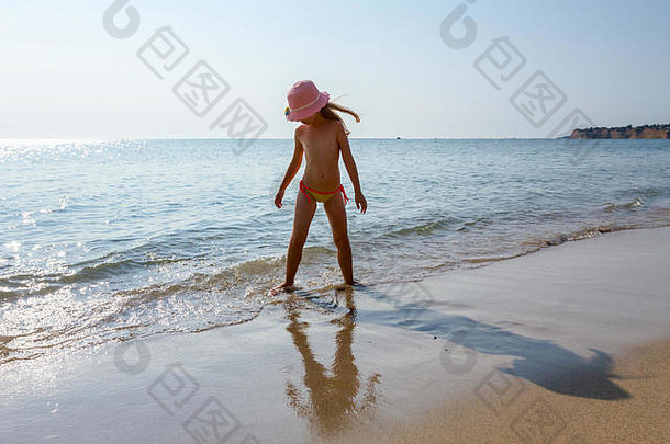 年轻的女人，戴着可爱的夏日帽子的不安的孩子，在浅水中跳舞，在海边的沙滩上嬉戏。