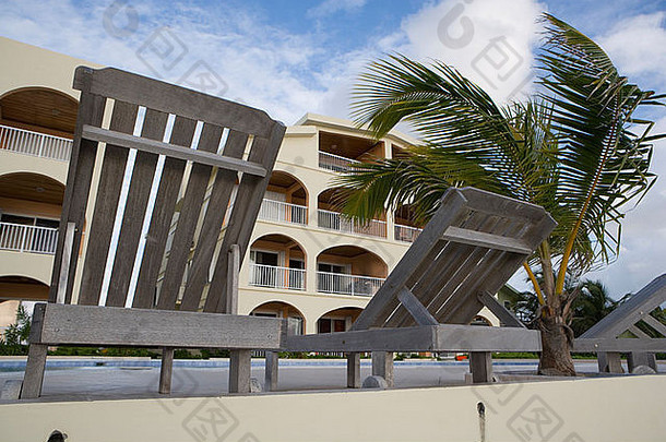 在墨西哥湾<strong>度假</strong>期间，木制休闲椅坐在泳池边，一棵小棕榈树在风中飘动。