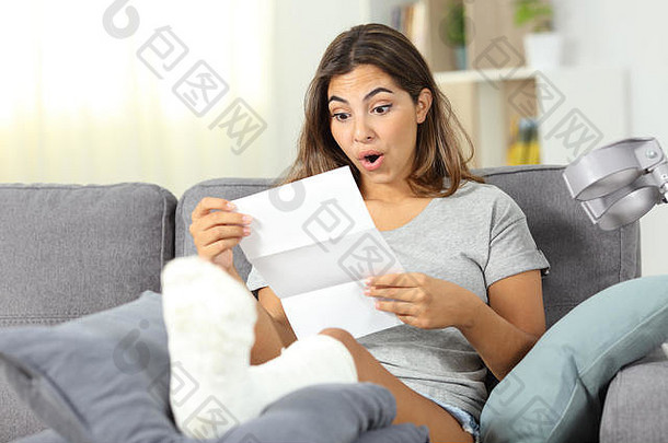 惊讶的残疾女孩坐在家客厅的沙发上阅读通知