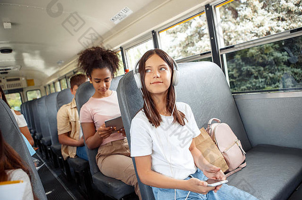 坐<strong>公交车上</strong>学的同学坐着戴着耳机的女孩特写镜头听音乐拿着智能手机微笑沉思