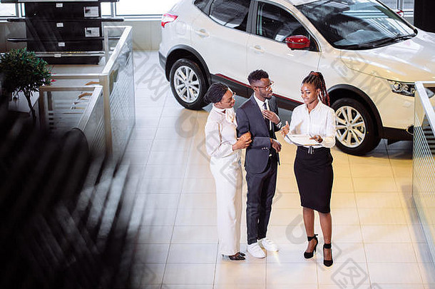 非洲汽车销售员站在经销商处向非洲夫妇客户讲述汽车功能的高角度视图