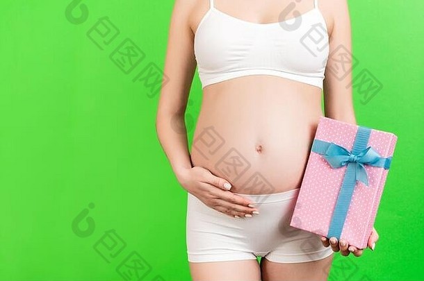 一张裁剪过的照片，照片中的孕妇穿着白色内衣，手持绿色背景的粉红色斑点礼盒。等待一个。复制空间。