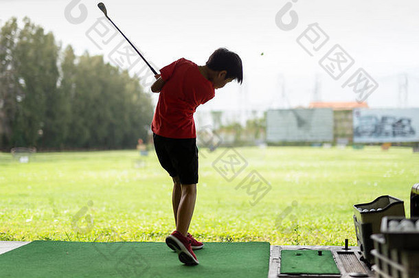 年轻的亚洲男孩正在高尔夫练习场练习挥杆。