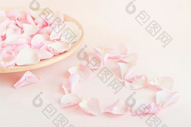 玫瑰花瓣心的柔和粉红像和装满粉红色玫瑰花瓣的木制盘子