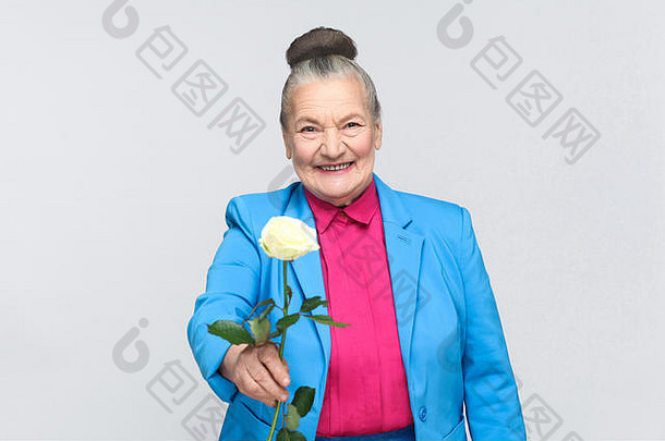 幸福老妇人送给你白玫瑰。穿着浅蓝色西装和粉红色衬衫，站着一位英俊、富于表情的祖母，她留着一个灰色的圆髻