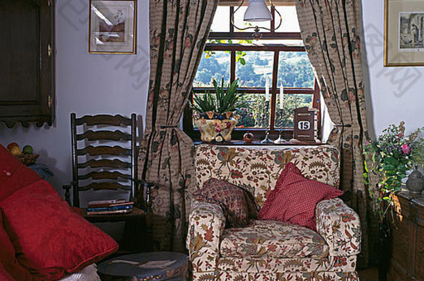 平房客厅花扶手椅上方的窗户上有图案窗帘，有古董梯子靠椅和彩绘圆形盒子