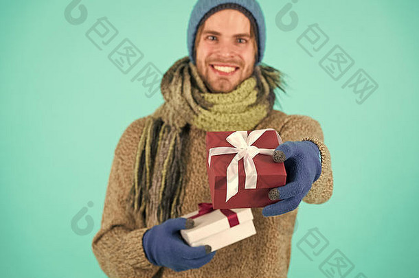 赶时髦的人持有圣诞节礼物弓假期现在概念冬天假期给礼物传播幸福男人。有胡子的英俊的穿冬天他围巾手套持有礼物盒子