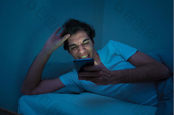 瘾<strong>君子</strong>深夜在床上用智能手机聊天和上网。在光线阴暗的房间里无聊、失眠、疲倦。在里面