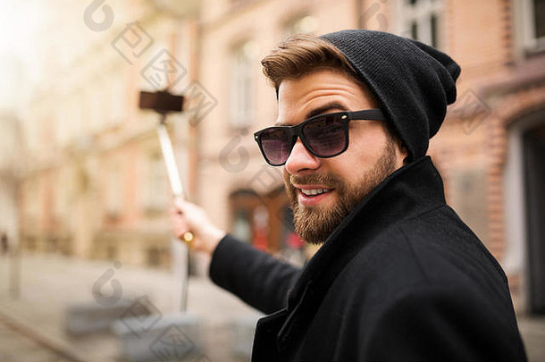 一张年轻时髦的男子用手机在<strong>自拍杆</strong>上拍照的照片。