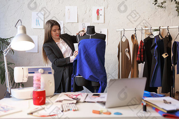 一位留着长发的女裁缝站在穿着蓝色布料的人体模特旁边的照片。