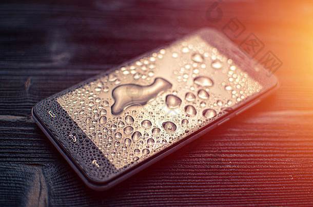 液体水滴在智能手机的玻璃上，落在木质桌面上