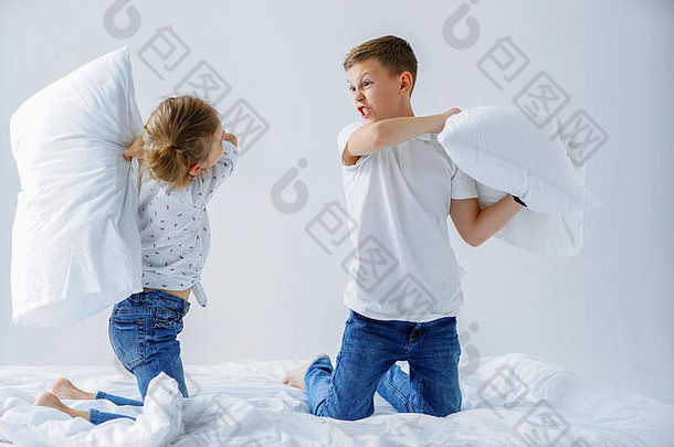 淘气的双胞胎女孩男孩友好的战斗上演了枕头战斗床上卧室种类游戏
