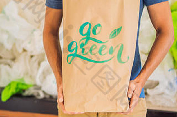 一名男子拿着一个写有铭文的包裹，在一堆塑料袋中变绿。零废物概念。世界环境日旗帜的概念，长