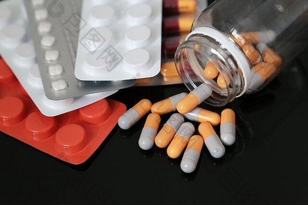 黑色玻璃桌上的药片、药片和胶囊从瓶子里散落。<strong>冠状病毒防护</strong>、药学、抗生素的概念