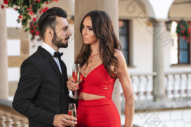 在豪华派对上，一对优雅的情侣站在阳台上，端着一杯葡萄酒或香槟。
