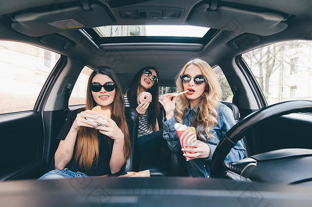 坐在车里，四位年轻、快乐、美丽的女士面带微笑地看着对方，一边吃着外卖