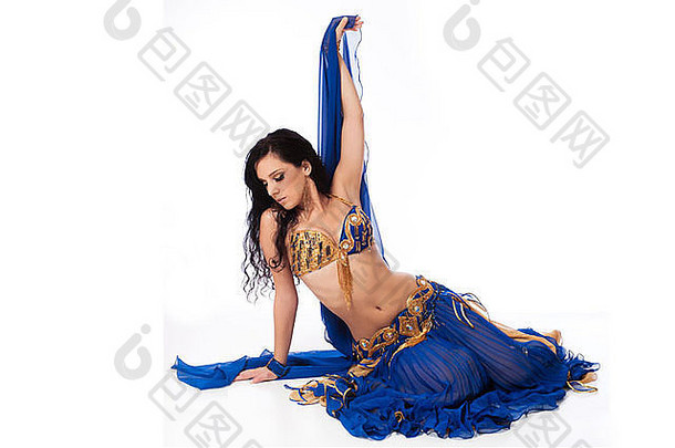 穿着蓝色服装的漂亮肚皮舞演员。她坐在地板上，一只手举着面纱。在whit上隔离